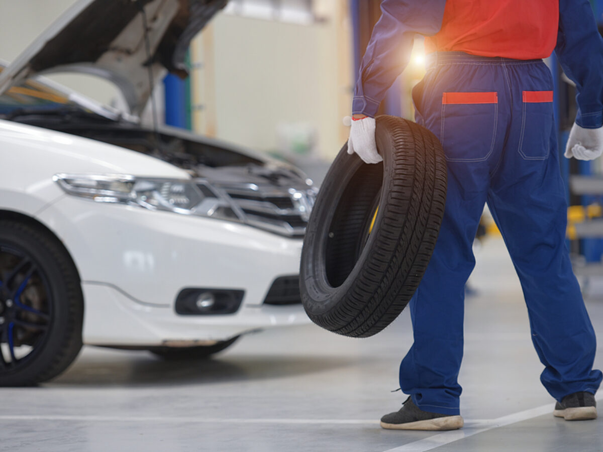 Handsome young auto mechanic in uniform is examining a tire while working in auto service Mechanic holding a tire tire at the repair garage replacement of winter and summer tires.